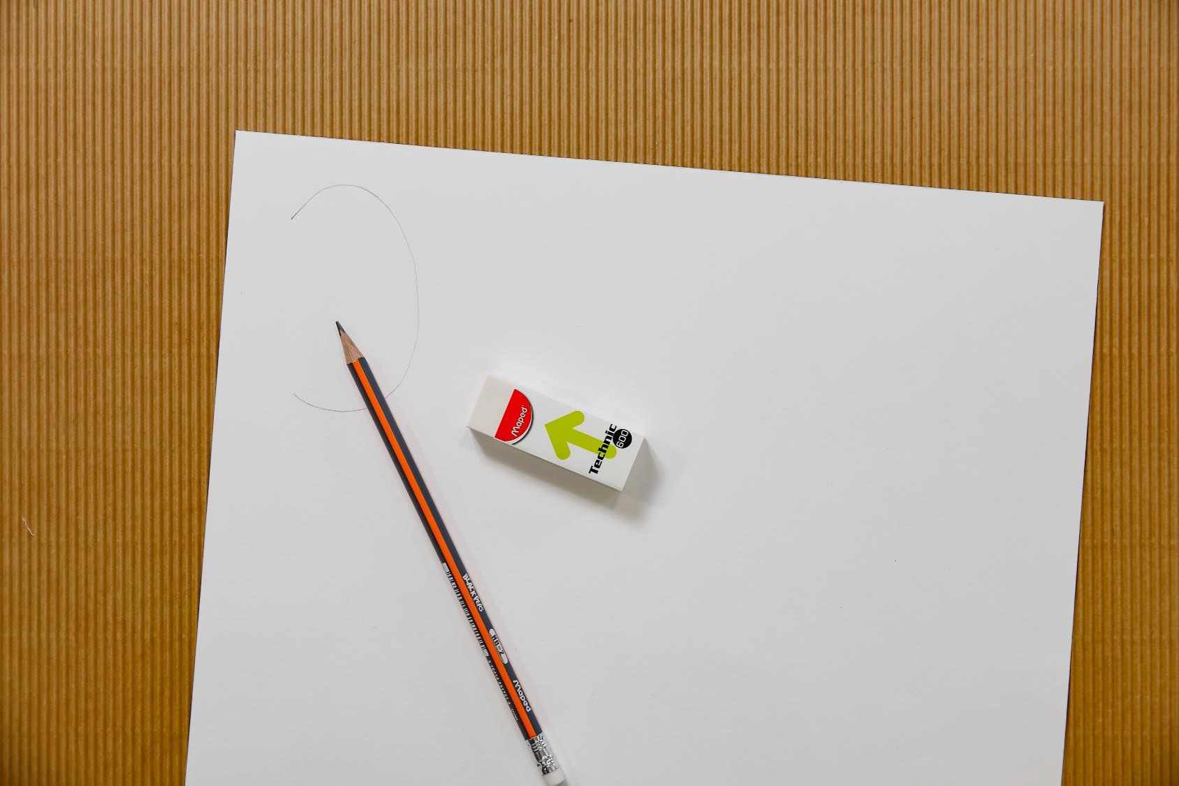 A plain white piece of paper laying on a desk with a pencil and eraser on top