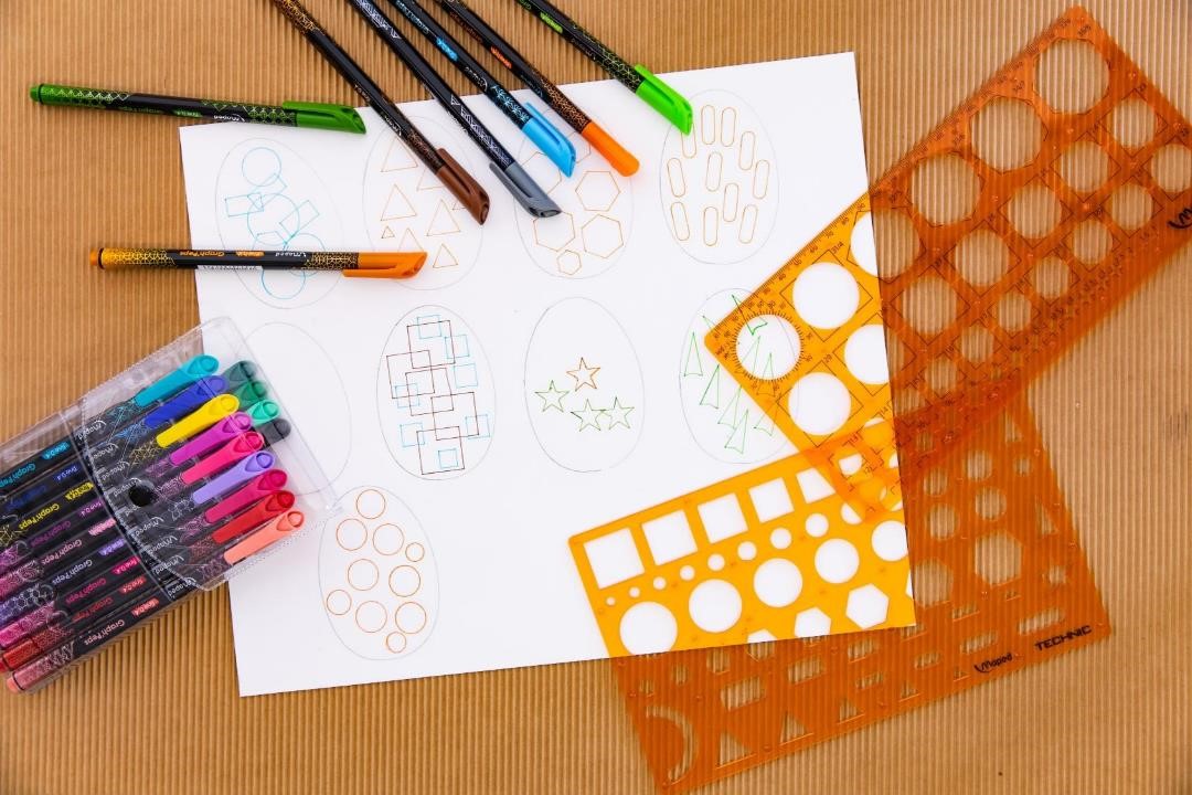 Hand drawn eggs decorated with geometric designs next to stencils and fineliners