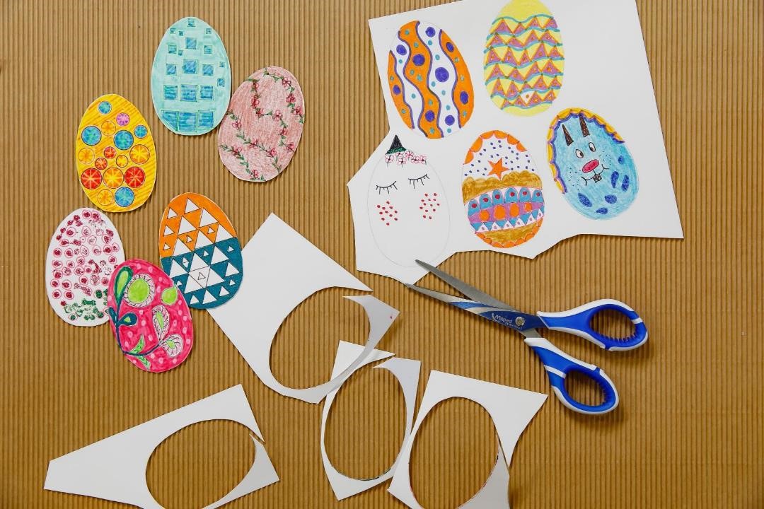 Scissors cutting out decorated paper eggs
