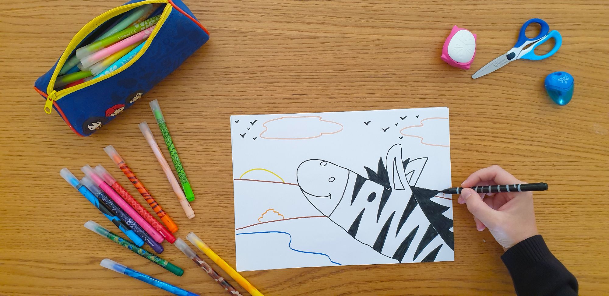 A piece of paper with a drawing of a zebra laying on a desk surrounded by stationery