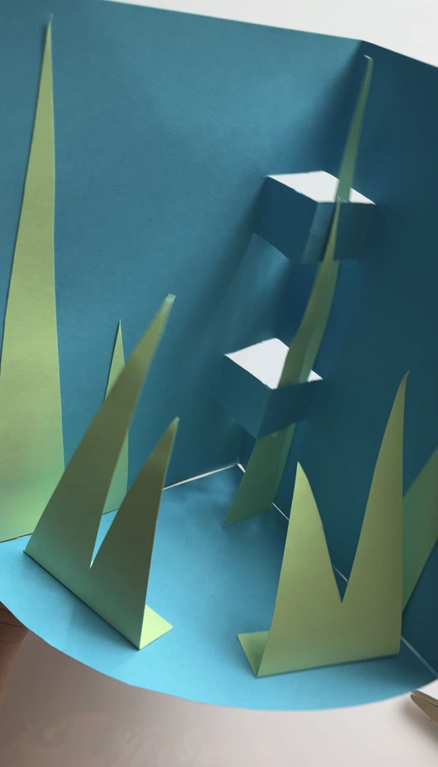Green paper leaves standing upright against the blue folded card