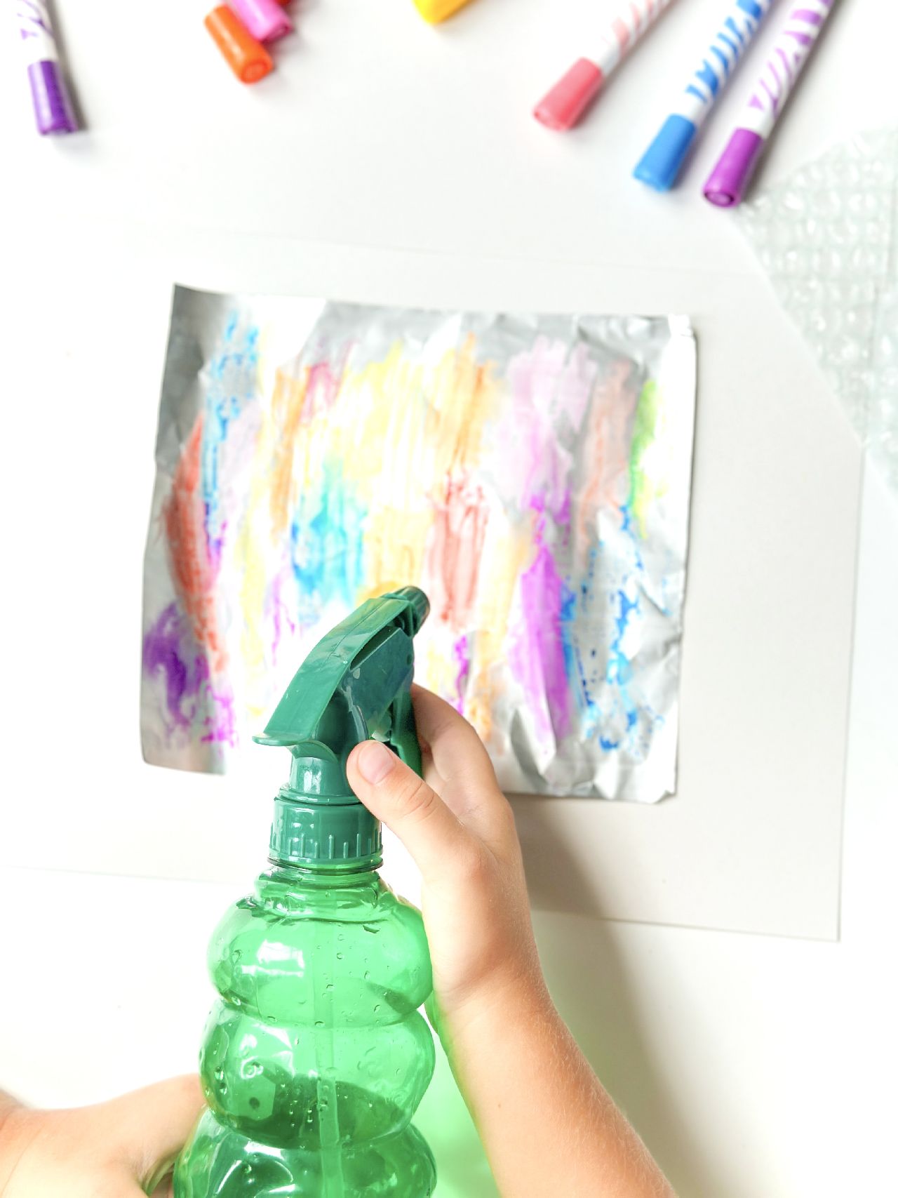 A sheet of foil that has been coloured in with felt pens with a hand holding a spray bottle